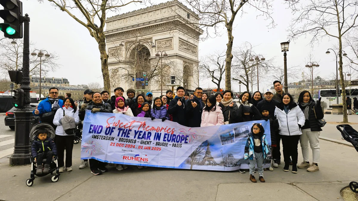 Grup perjalanan Ruhens memegang spanduk di depan Arc de Triomphe di Paris.