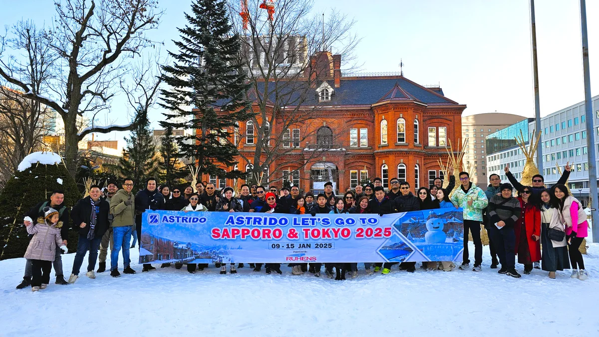 Grup perjalanan Ruhens dengan spanduk di depan bangunan bata merah di Sapporo yang bersalju.