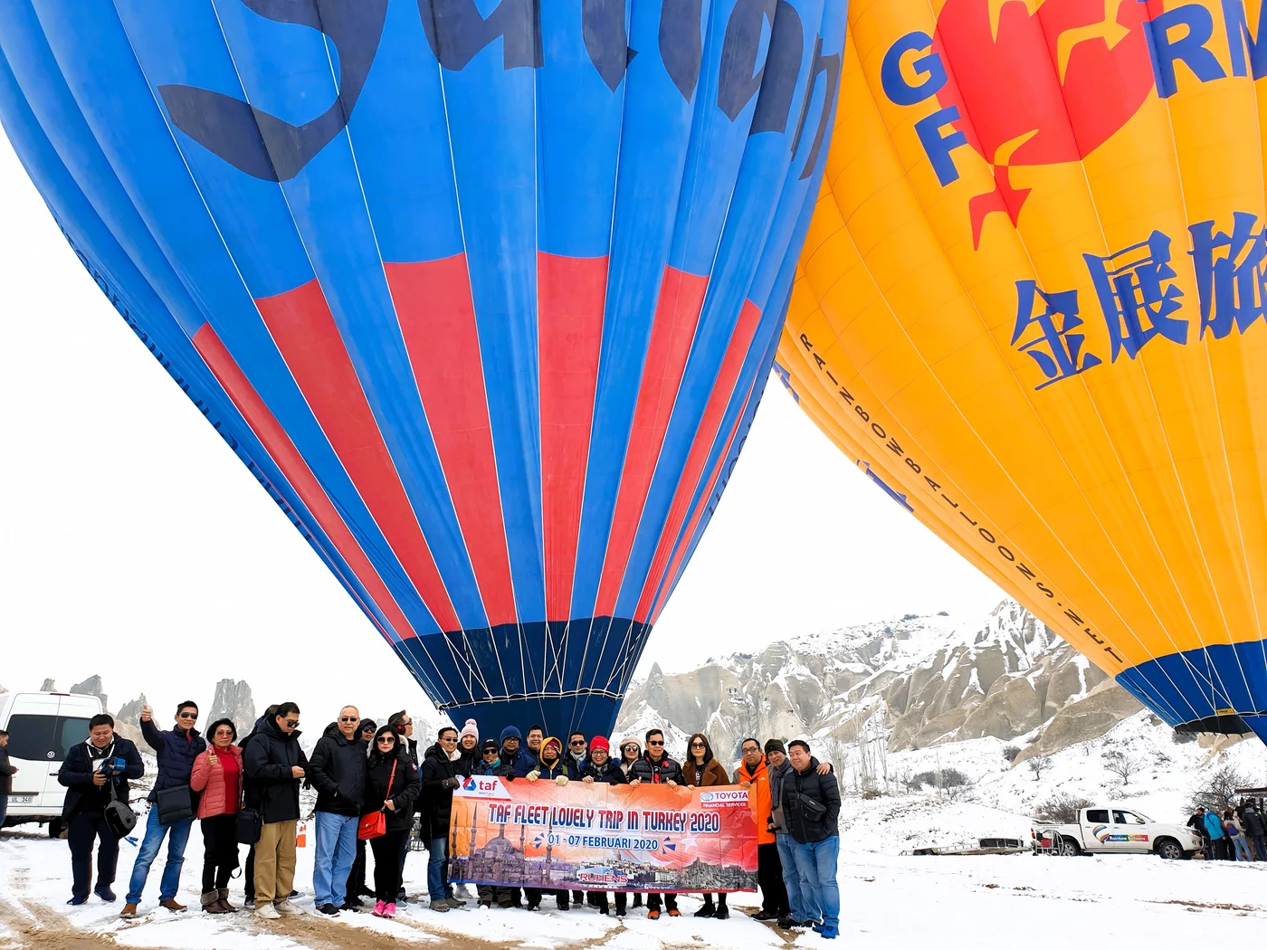 Peserta perjalanan Ruhens dengan spanduk grup di bawah balon udara berwarna-warni di lanskap bersalju Türkiye.