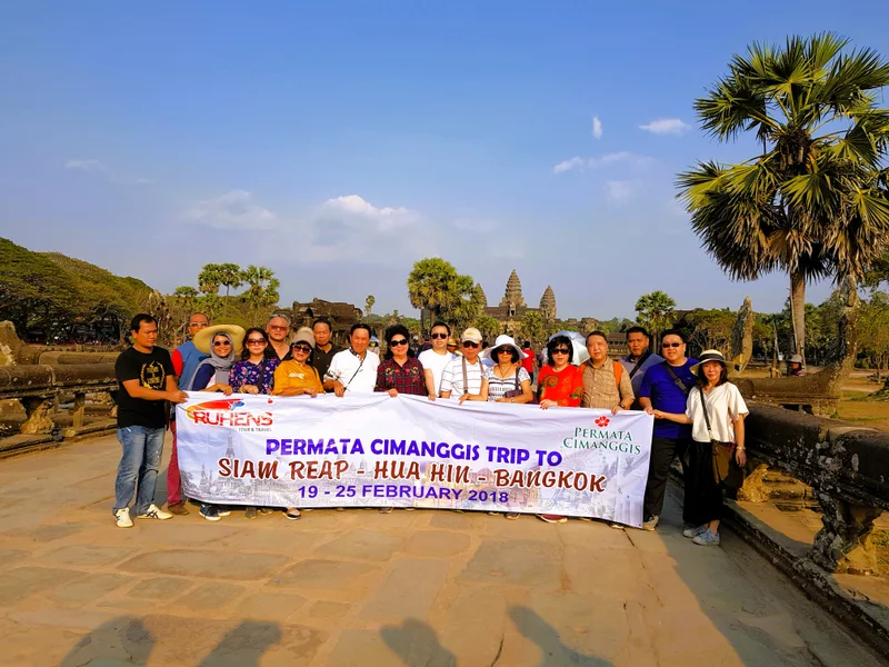 Grup perjalanan Ruhens dengan spanduk di depan candi dan pepohonan palem.