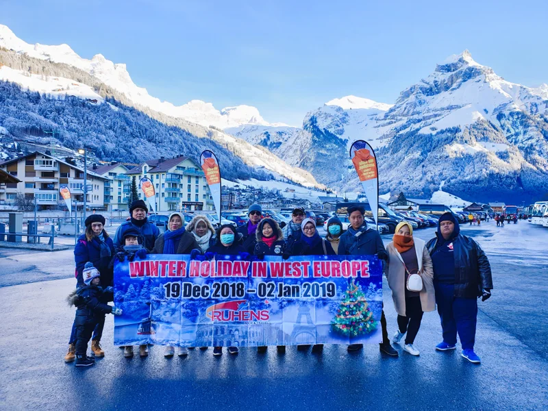 Grup perjalanan Ruhens dengan spanduk di depan pegunungan dan desa bersalju.