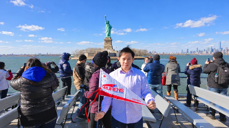 Seorang peserta memegang bendera Ruhens dengan Patung Liberty di belakangnya di New York.