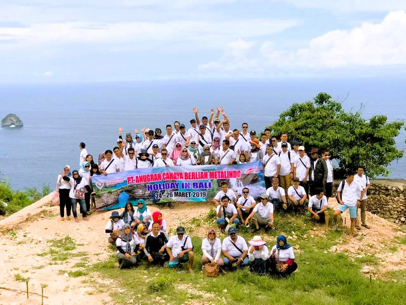 Grup Metalindo dengan spanduk berfoto di bukit pesisir Bali dengan laut di belakangnya.