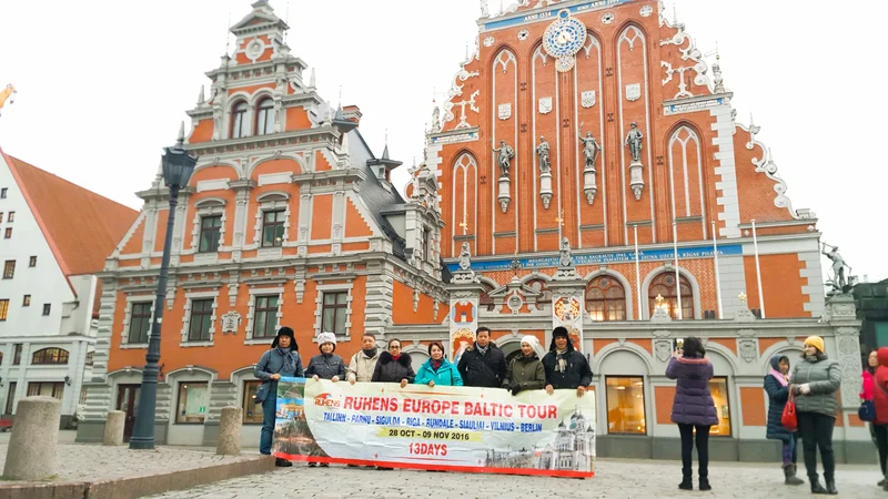 Grup perjalanan dengan spanduk Ruhens Europe Baltic Tour berfoto di depan bangunan bersejarah berwarna merah.