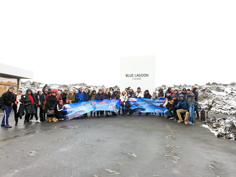 Grup perjalanan dengan spanduk Agung Toyota berfoto di depan papan Blue Lagoon Iceland di lanskap bersalju.