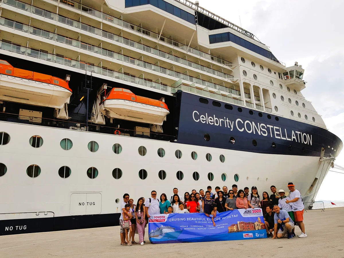 Grup perjalanan dengan spanduk Auto 2000 berfoto di depan kapal pesiar Celebrity Constellation.