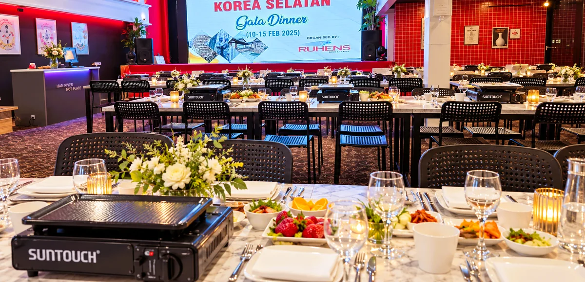 Ruang gala dinner dengan meja tertata, bunga, dan layar acara Korea Selatan.